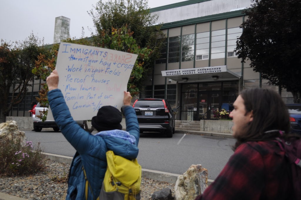 An immigration activist holds a sign outside the Kittitas County Courthouse Sept. 29, 2019, challenging Sheriff Gene Dana’s legacy as the longest-serving sheriff in Washington. Immigration rights advocates called on Dana to cancel a contract with Immigration and Customs Enforcement before his retirement in October. CREDIT: CREDIT: Enrique Pérez de la Rosa/NWPB