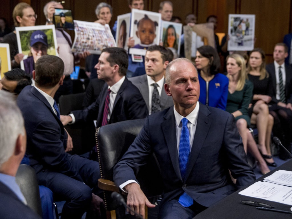 Boeing Company President and Chief Executive Officer Dennis Muilenburg (right foreground) with hearing attendees holding up photographs of those killed in the Ethiopian Airlines Flight 302 and Lion Air Flight 610 crashes. CREDIT: Andrew Harnik/AP