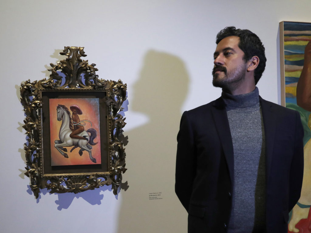 Mexican artist Fabián Cháirez stands next to his painting of Mexican revolutionary hero Emiliano Zapata, straddling a horse nude, wearing high heels and a pink hat, at the Fine Arts Palace in Mexico City on Dec. 11, 2019. CREDIT: Marco Ugarte/AP