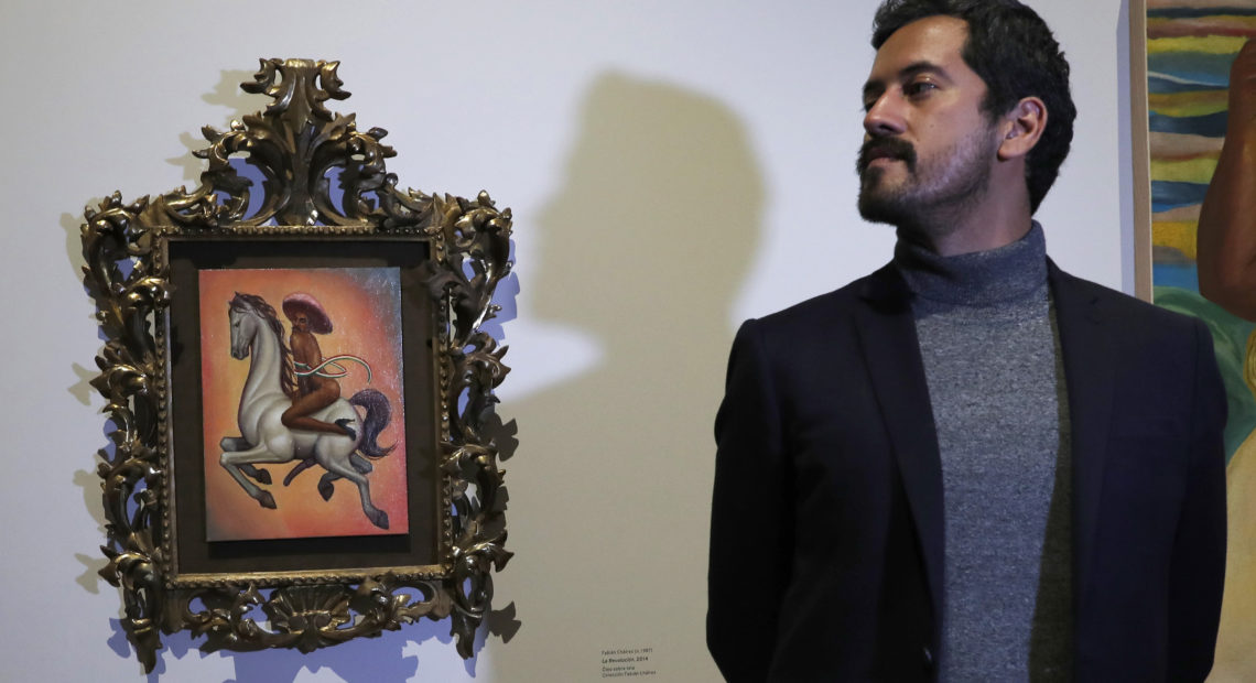 Mexican artist Fabián Cháirez stands next to his painting of Mexican revolutionary hero Emiliano Zapata, straddling a horse nude, wearing high heels and a pink hat, at the Fine Arts Palace in Mexico City on Dec. 11, 2019. CREDIT: Marco Ugarte/AP