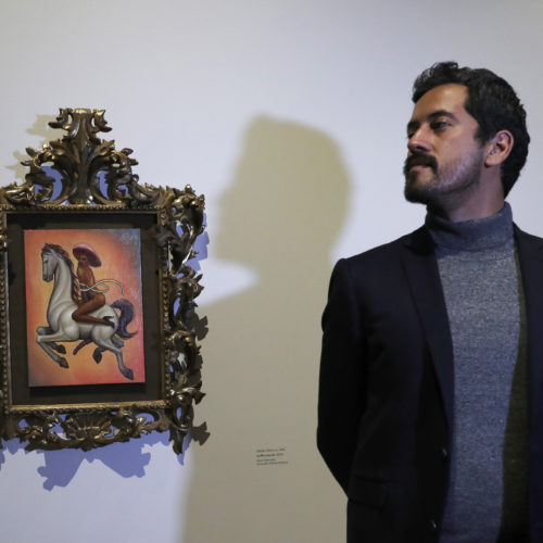 Mexican artist Fabián Cháirez stands next to his painting of Mexican revolutionary hero Emiliano Zapata, straddling a horse nude, wearing high heels and a pink hat, at the Fine Arts Palace in Mexico City on Dec. 11, 2019. CREDIT: Marco Ugarte/AP