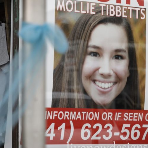 File photo. A 2018 poster for then-missing University of Iowa student Mollie Tibbetts hangs in the window of a local business in Brooklyn, Iowa. Regulators are proposing a nearly $13 million fine against Scott Rhodes, who they say illegally hid the origin of automated phone calls that used the slaying of Tibbetts, and election campaigns in other states to promote white nationalist and anti-Semitic messages. CREDIT: Charlie Neibergall / AP