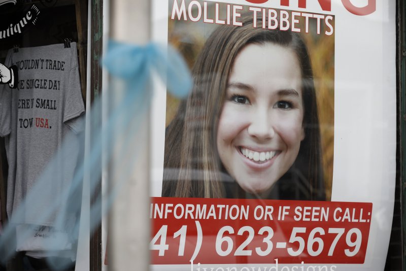 File photo. A 2018 poster for then-missing University of Iowa student Mollie Tibbetts hangs in the window of a local business in Brooklyn, Iowa. Regulators are proposing a nearly $13 million fine against Scott Rhodes, who they say illegally hid the origin of automated phone calls that used the slaying of Tibbetts, and election campaigns in other states to promote white nationalist and anti-Semitic messages. CREDIT: Charlie Neibergall / AP