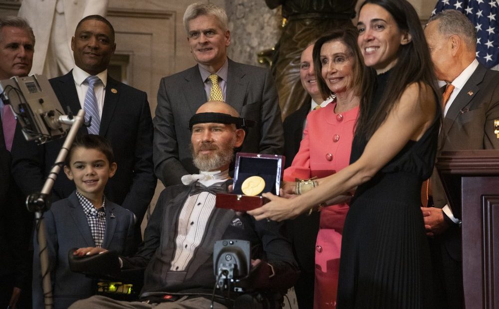 A Congressional Gold Medal is presented to amyotrophic lateral sclerosis (ALS) advocate and former National Football League (NFL) player, Steve Gleason, in Statuary Hall on Capitol Hill, Jan. 15, 2020. Holding the medal is his wife Michel Gleason. CREDIT: Manuel Balce Ceneta/AP