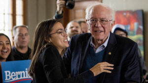 Sen. Bernie Sanders smiles as he is welcomed to the podium by Rep. Alexandria Ocasio-Cortez of New York during a campaign stop in Perry, Iowa
