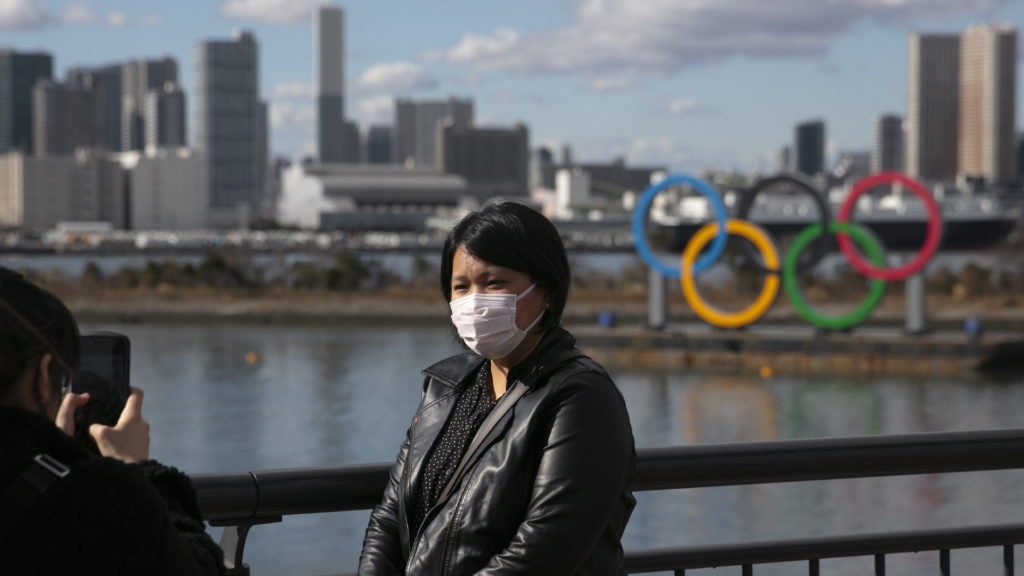 A tourist wearing a mask poses for a photo with the Olympic rings in the background, at Tokyo's Odaiba district, in a photo taken last month. Jae C. Hong/AP