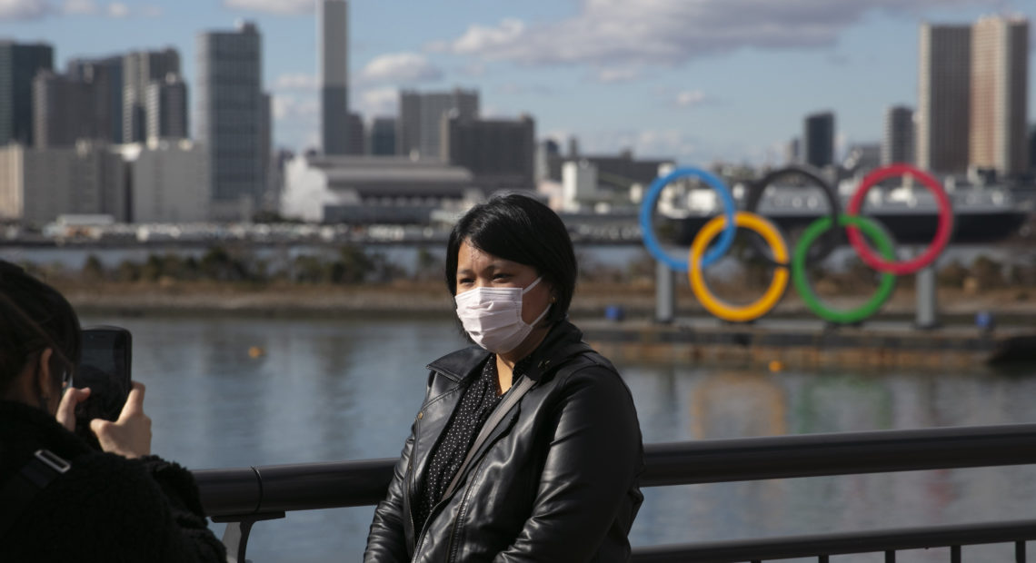 A tourist wearing a mask poses for a photo with the Olympic rings in the background, at Tokyo's Odaiba district, in a photo taken last month. Jae C. Hong/AP