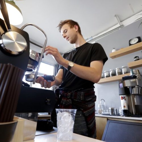 File photo. Porter Hahn makes an iced coffee drink in November 2019 in a Seattle coffee shop. U.S. services companies grew at a faster pace in February 2020 than the previous month. Then the coronavirus outbreak in the region shut down much of the service industry. CREDIT: Elaine Thompson/AP