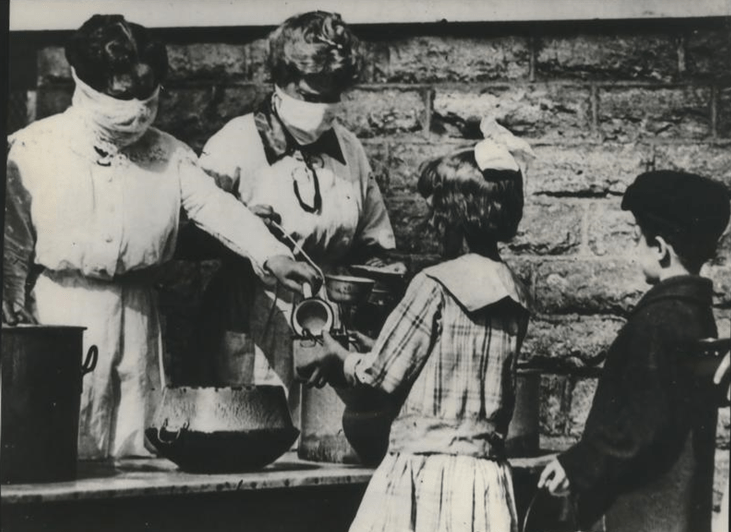 Volunteers wearing gauze masks at a street kitchen in Cincinnati serve food to children of families afflicted by the flu pandemic in the winter of 1918-1919.