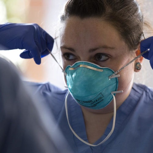 Jess White, a registered nurse at UW Northwest, demonstrates to another nurse how to properly remove a mask on Thursday, March 12, 2020, at UW Medicine's drive-through testing clinic in Seattle. CREDIT: Megan Farmer/KUOW