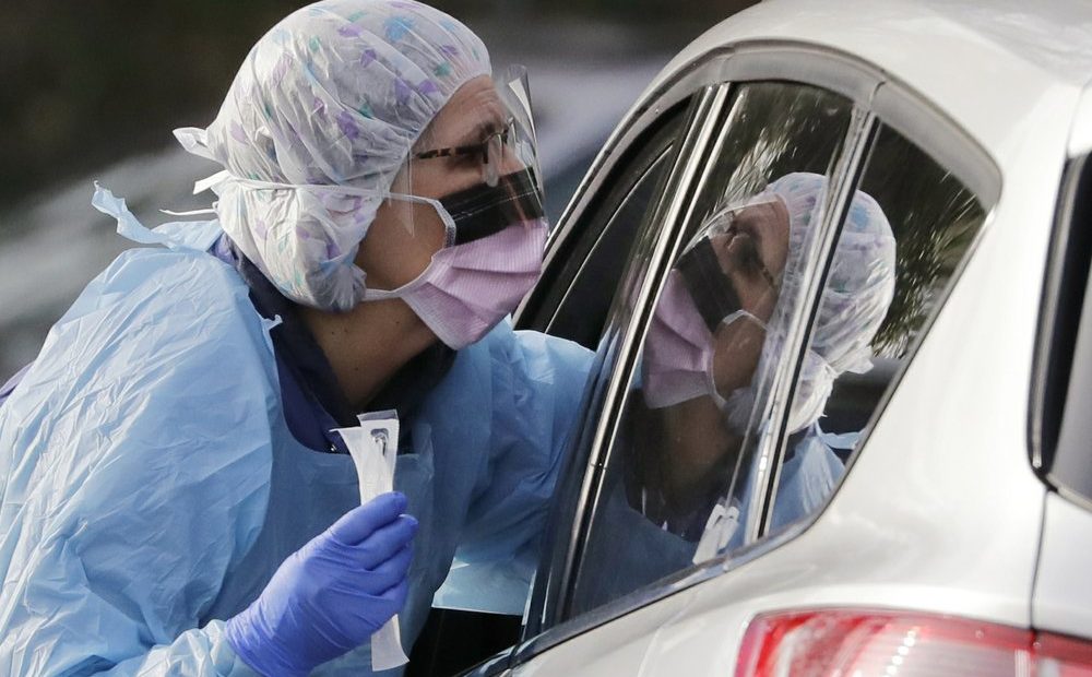Laurie Kuypers, a registered nurse, reaches into a car to take a swab from a patient at a drive-through COVID-19 coronavirus testing station for University of Washington Medicine. The federal government is trying to get more protective equipment to states for medical workers who will be on the front lines of the growing coronavirus pandemic. CREDIT: Elaine Thompson/AP