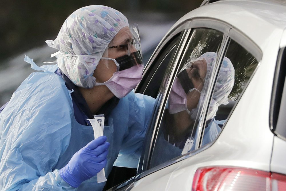 Laurie Kuypers, a registered nurse, reaches into a car to take a swab from a patient at a drive-through COVID-19 coronavirus testing station for University of Washington Medicine. The federal government is trying to get more protective equipment to states for medical workers who will be on the front lines of the growing coronavirus pandemic. CREDIT: Elaine Thompson/AP