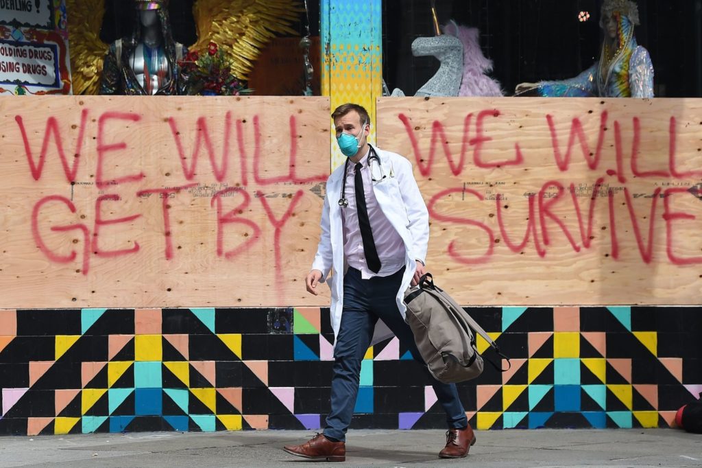 Stuart Malcolm, a doctor with the Haight Ashbury Free Clinic, walks by a supportive sign on a boarded-up shop in San Francisco on Tuesday. NPR is launching The National Conversation with NPR's All Things Considered where we're going to have experts answer your questions about the coronavirus. CREDIT: Josh Edelson/AFP via Getty Images