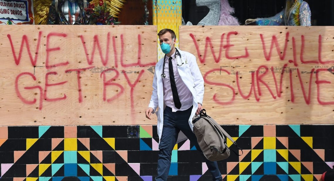 Stuart Malcolm, a doctor with the Haight Ashbury Free Clinic, walks by a supportive sign on a boarded-up shop in San Francisco on Tuesday. NPR is launching The National Conversation with NPR's All Things Considered where we're going to have experts answer your questions about the coronavirus. CREDIT: Josh Edelson/AFP via Getty Images