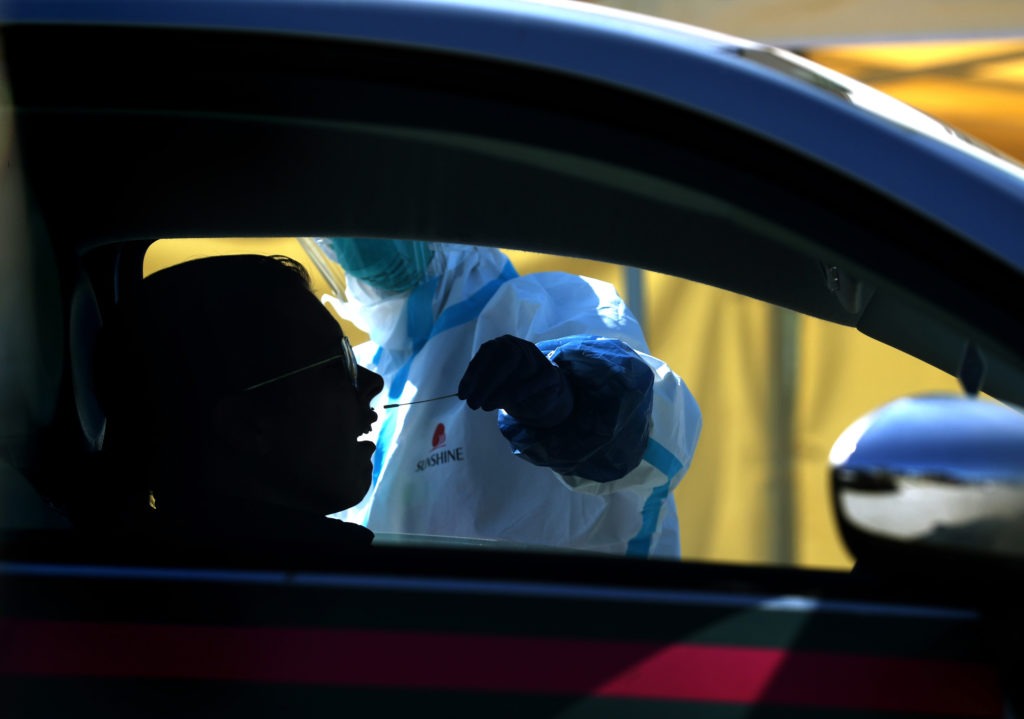 After an initial verbal screening, one driver at a time gets a COVID-19 nasal swab test from a garbed health worker at a drive-up station in Daly City, Calif. Justin Sullivan/Getty Images