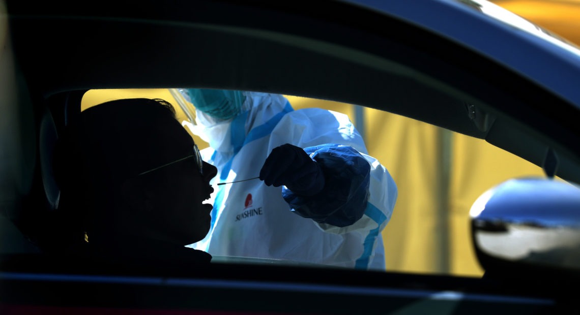 After an initial verbal screening, one driver at a time gets a COVID-19 nasal swab test from a garbed health worker at a drive-up station in Daly City, Calif. Justin Sullivan/Getty Images