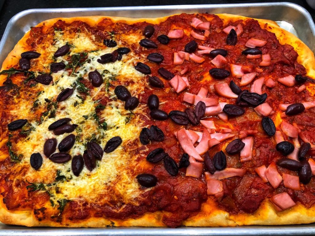 A fully cooked example of King's Grandma's Pizza Doug Recipe with half black olives and ham and half black olives and cheese.