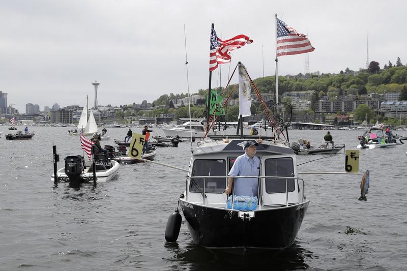 A protester reels in a fake fish near poles marking a six-foot social distance on a boat on Lake Union in Seattle April 26, 2020 during a protest against Washington state's current ban on recreational fishing. CREDIT: Ted S. Warren/AP