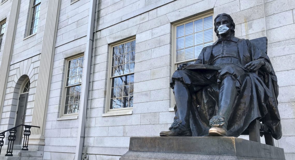 A statue of John Harvard wears a face mask