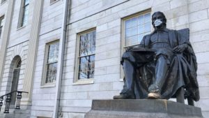 A statue of John Harvard wears a face mask