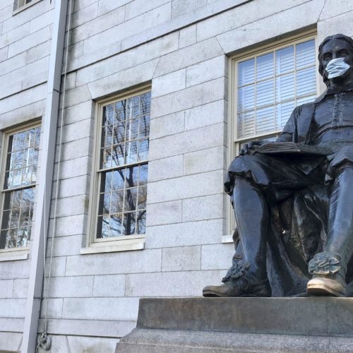 A statue of John Harvard wears a face mask