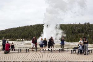 Visitors watch as Old Faithful erupts on the day the park partially reopened after a two-month shutdown due to the coronavirus pandemic, at Yellowstone National Park, Wyo. Officials at Yellowstone and other national parks plan to let tourists mostly police themselves and not intervene much to enforce social distancing.