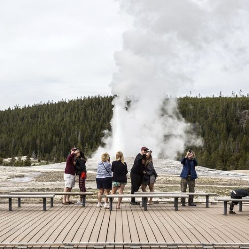 Visitors watch as Old Faithful erupts on the day the park partially reopened after a two-month shutdown due to the coronavirus pandemic, at Yellowstone National Park, Wyo. Officials at Yellowstone and other national parks plan to let tourists mostly police themselves and not intervene much to enforce social distancing.