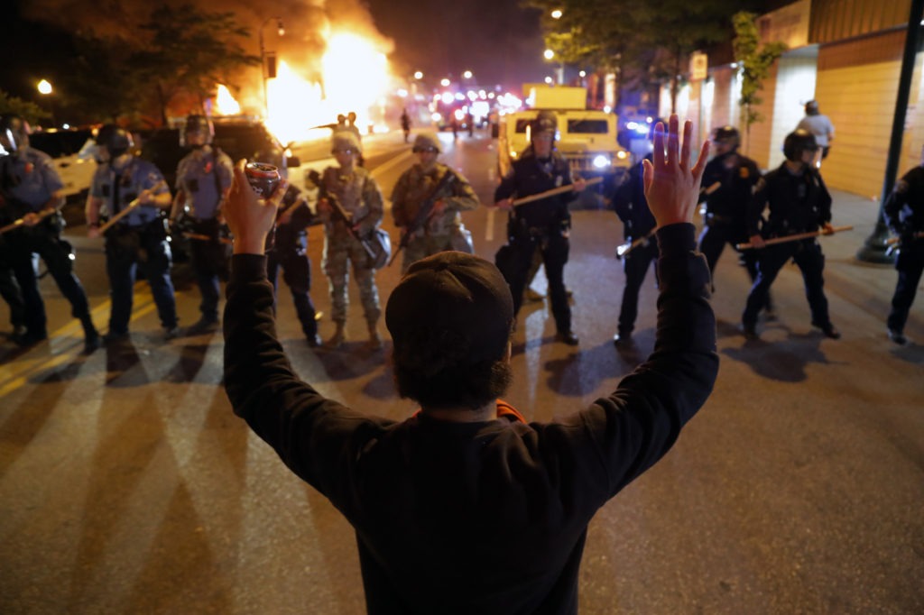 A man raises his hands as police line up across the street during protests Friday in Minneapolis. Demonstrators expressed outrage and grief across the nation over the death of George Floyd, a black man who was killed by police. CREDIT: Julio Cortez/AP