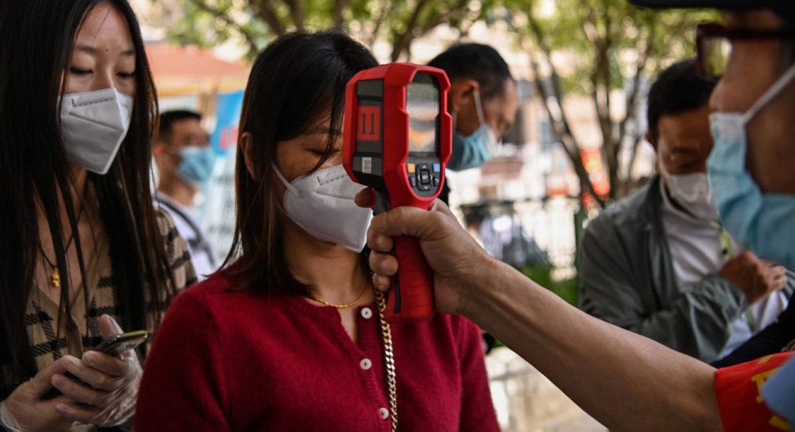 A worker checks a passenger's body temperature on Tuesday after arriving in Wuhan, China.
