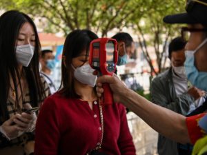 A worker checks a passenger's body temperature on Tuesday after arriving in Wuhan, China.