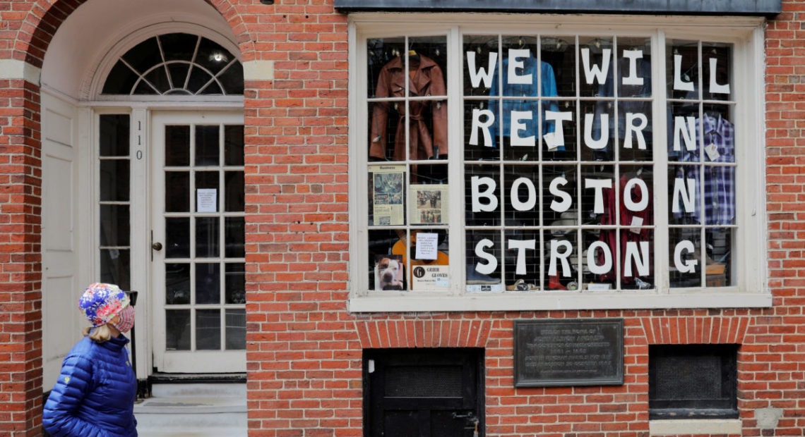 A pedestrian walks past a sign in a shop window reading "We Will Return Boston Strong" after Massachusetts Governor Charlie Baker extended his stay-at-home advisory and his order closing non-essential businesses