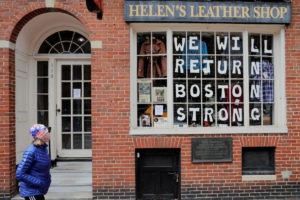 A pedestrian walks past a sign in a shop window reading "We Will Return Boston Strong" after Massachusetts Governor Charlie Baker extended his stay-at-home advisory and his order closing non-essential businesses