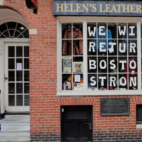 A pedestrian walks past a sign in a shop window reading "We Will Return Boston Strong" after Massachusetts Governor Charlie Baker extended his stay-at-home advisory and his order closing non-essential businesses