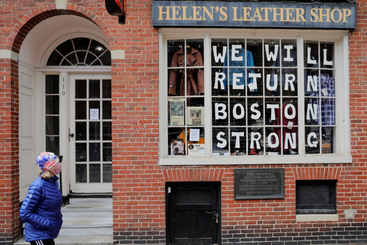 A pedestrian walks past a sign in a shop window reading "We Will Return Boston Strong" after Massachusetts Governor Charlie Baker extended his stay-at-home advisory and his order closing non-essential businesses