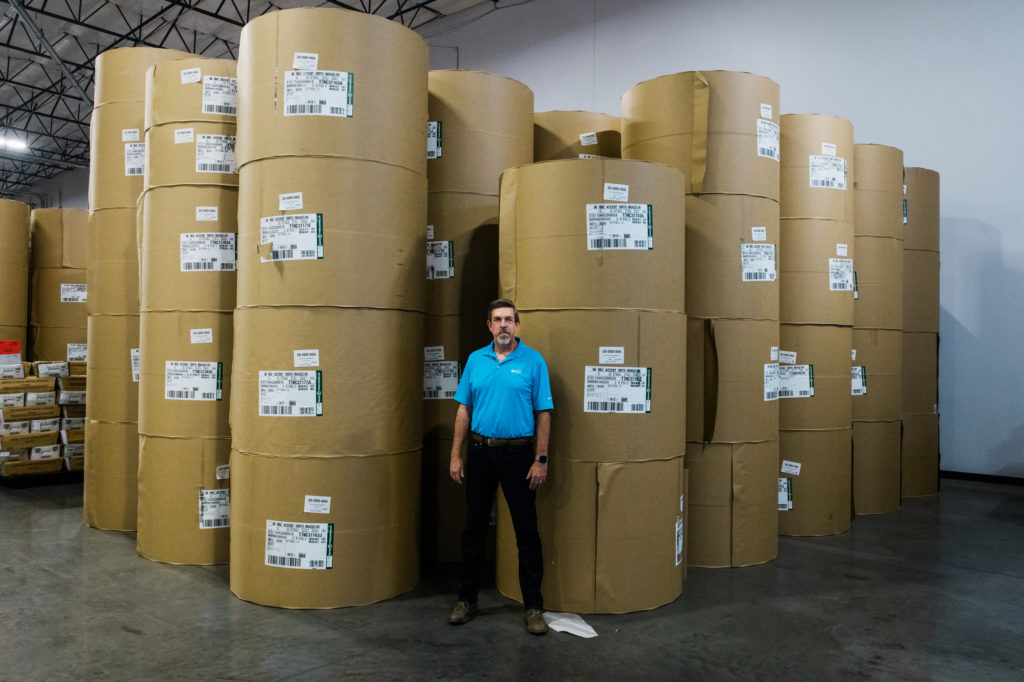 Jeff Ellington, president and COO of Runbeck Election Services, stands in front of massive rolls of paper used to create mail-in ballots. Ash Ponders for NPR