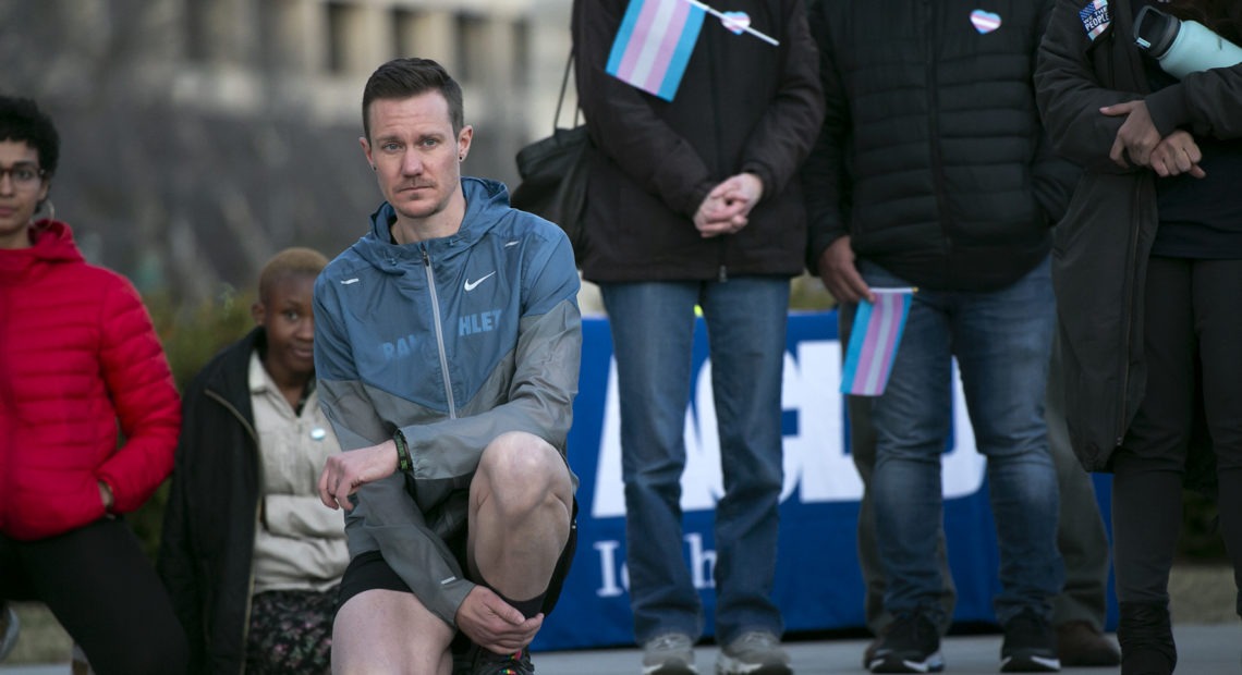Chris Mosier, a Team USA athlete and transgender activist, kneels as he listens to speakers at a rally at the Statehouse on Tuesday, March 3 against Idaho’s HB500 banning transgender athletes from participating in women’s sports.