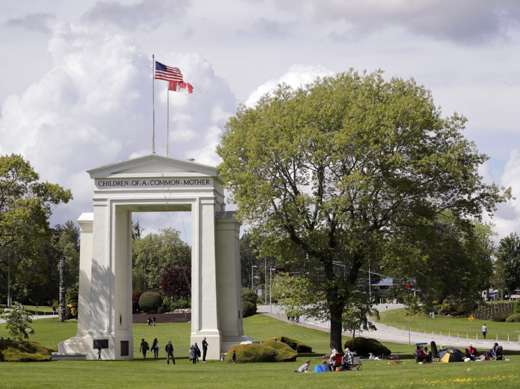 People walk back and forth across the border between the U.S. and Canada in Peace Arch Park in Blaine, Wash., on May 17, 2020. With the border closed to nonessential travel amid the global pandemic, families and couples across the continent found themselves cut off from loved ones on the other side. The park reopening reunited many of them. CREDIT: Elaine Thompson/AP