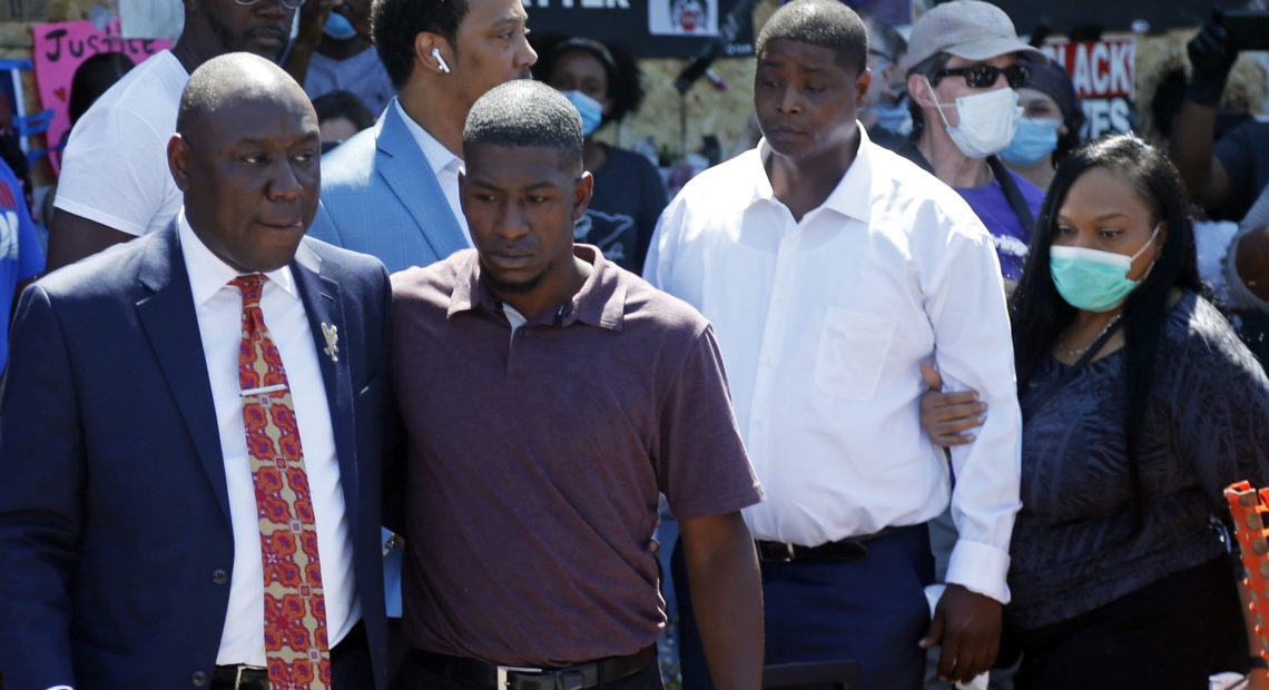 All four former Minneapolis police officers now face criminal charges in the death of George Floyd. Attorney Ben Crump, left, escorts Floyd's son Quincy Mason, second from left, on Wednesday during a visit to the memorial where Floyd was arrested in Minneapolis.