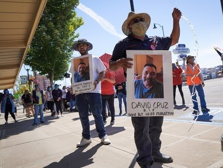 Farmworkers in Yakima's fruit-packing industry walked off production lines in May and went on strike, demanding more protections against the coronavirus pandemic. Above, Emmanuel Anguiano-Mendoza (left) and Agustin López hold posters featuring David Cruz, a worker who died on May 30. CREDIT: Enrique Pérez de la Rosa/NWPB