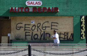 A mail carrier walks by a boarded-up business in the ethnically diverse Frogtown neighborhood of St. Paul, Minn., during continued demonstrations against the killing of George Floyd. 