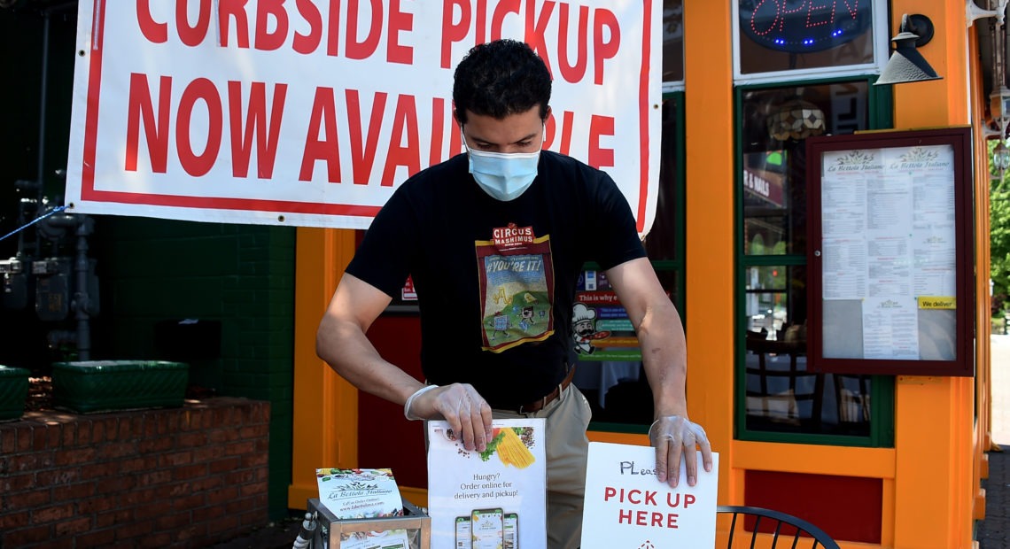 An employee sets a table for pickup orders at a restaurant in Arlington, Va. Even as states are moving to reopen their economies, tens of millions are out of work. CREDIT: Olivier Douliery/AFP via Getty Images