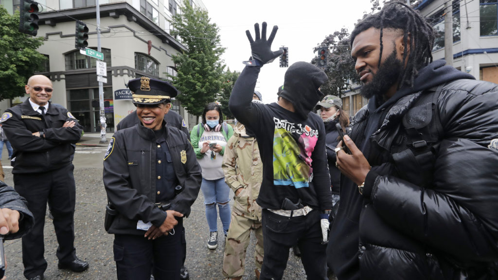Seattle Police Chief Carmen Best (saecond from left) talks this week with activists Raz Simone (right) and Keith Brown near the spot in the "Capitol Hill Autonomous Zone" where police had earlier boarded up a precinct building. CREDIT: Elaine Thompson/AP