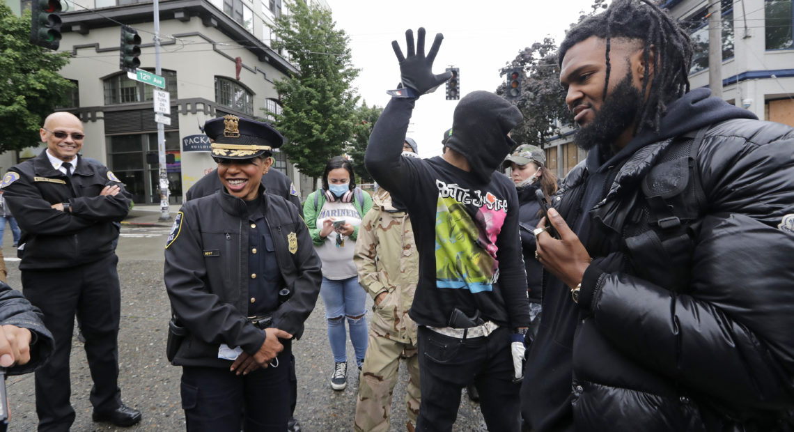 Seattle Police Chief Carmen Best (saecond from left) talks this week with activists Raz Simone (right) and Keith Brown near the spot in the "Capitol Hill Autonomous Zone" where police had earlier boarded up a precinct building. CREDIT: Elaine Thompson/AP