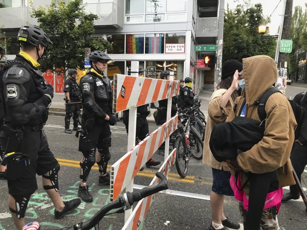 Protesters stand across from Seattle officers early Wednesday, July 1 in a road in the Capitol Hill Organized Protest zone. Police started taking down demonstrators' tents in the protest zone after Seattle's mayor ordered it to be cleared. CREDIT: Aron Ranen/AP