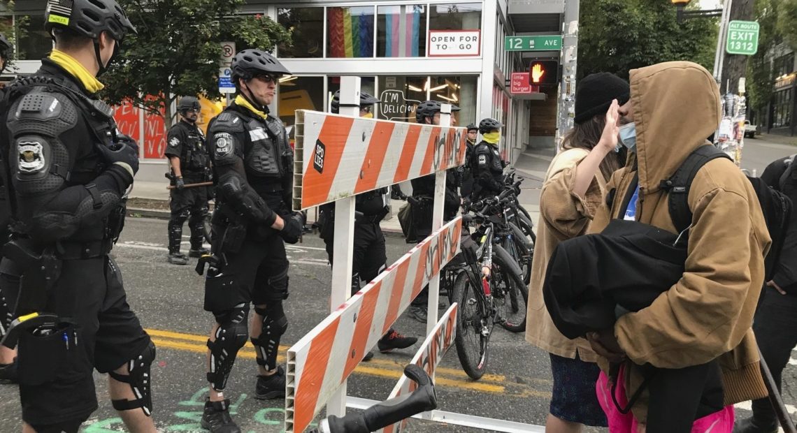Protesters stand across from Seattle officers early Wednesday, July 1 in a road in the Capitol Hill Organized Protest zone. Police started taking down demonstrators' tents in the protest zone after Seattle's mayor ordered it to be cleared. CREDIT: Aron Ranen/AP