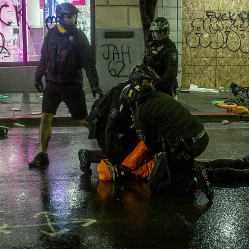 Bystanders yell at a police officer to remove his knee from a detained person’s neck while SPD made arrests at a vandalized T-Mobile store downtown, May 30, 2020. A moment later a fellow officer forcibly removed the officer's knee from the man's neck. CREDIT: Shaminder Dulai/Crosscut