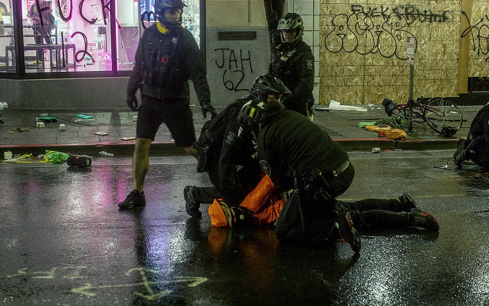 Bystanders yell at a police officer to remove his knee from a detained person’s neck while SPD made arrests at a vandalized T-Mobile store downtown, May 30, 2020. A moment later a fellow officer forcibly removed the officer's knee from the man's neck. CREDIT: Shaminder Dulai/Crosscut