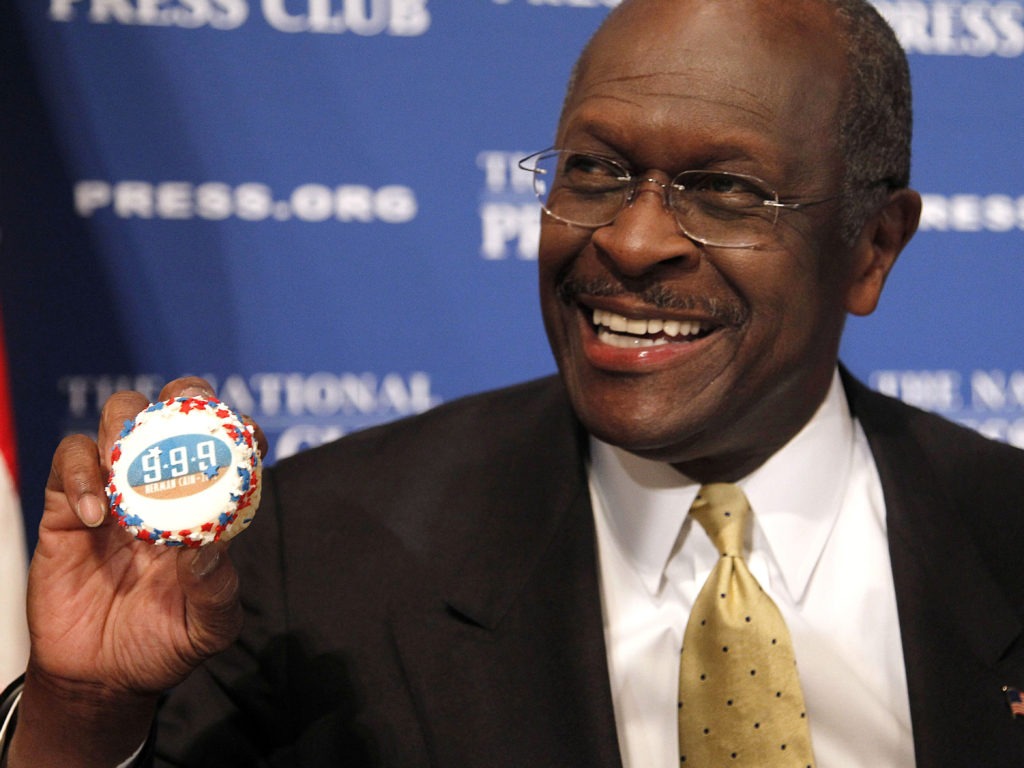 Herman Cain, then a GOP presidential candidate, holds a muffin bearing his catchphrase "9-9-9" tax plan at the National Press Club in Washington in 2011. Cain's death was announced Thursday. CREDIT: Pablo Martinez Monsivais/AP