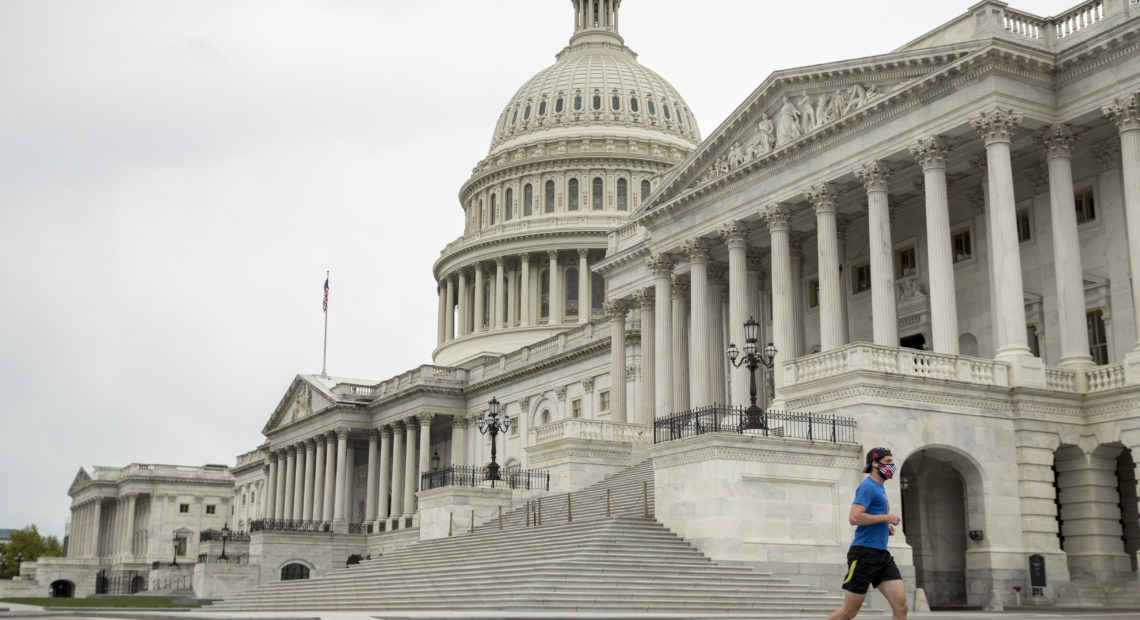 A man with a mask depicting American flags jogs past the U.S. Capitol in April. More than three-quarters of respondents to the NPR/Ipsos poll support enacting state laws to require mask wearing in public at all times. CREDIT: Andrew Harnik/AP