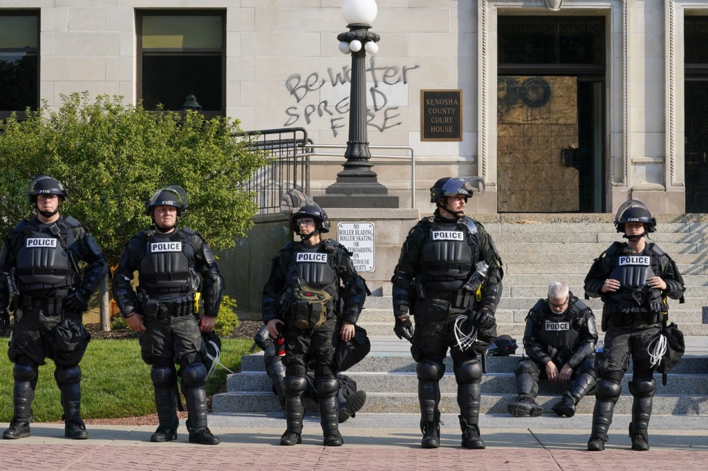 Police in riot gear stand outside the Kenosha County Court House Monday, in Kenosha, Wis. Kenosha police shot a man Sunday evening, setting off unrest in the city after a video appeared to show the officer firing several shots at close range into Jacob Blake back. CREDIT: Morry Gash/AP
